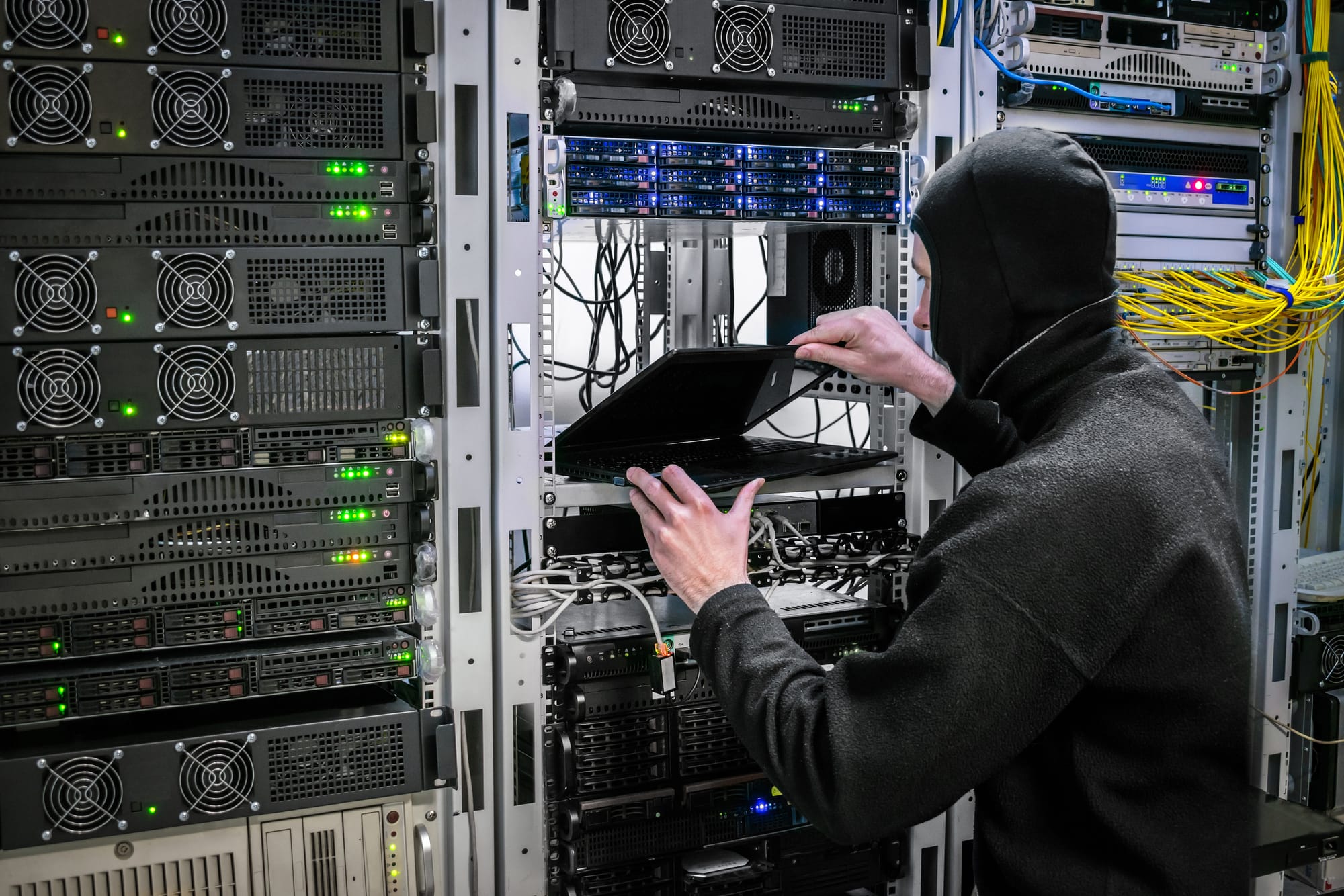cybercriminal accessing server rack with a laptop